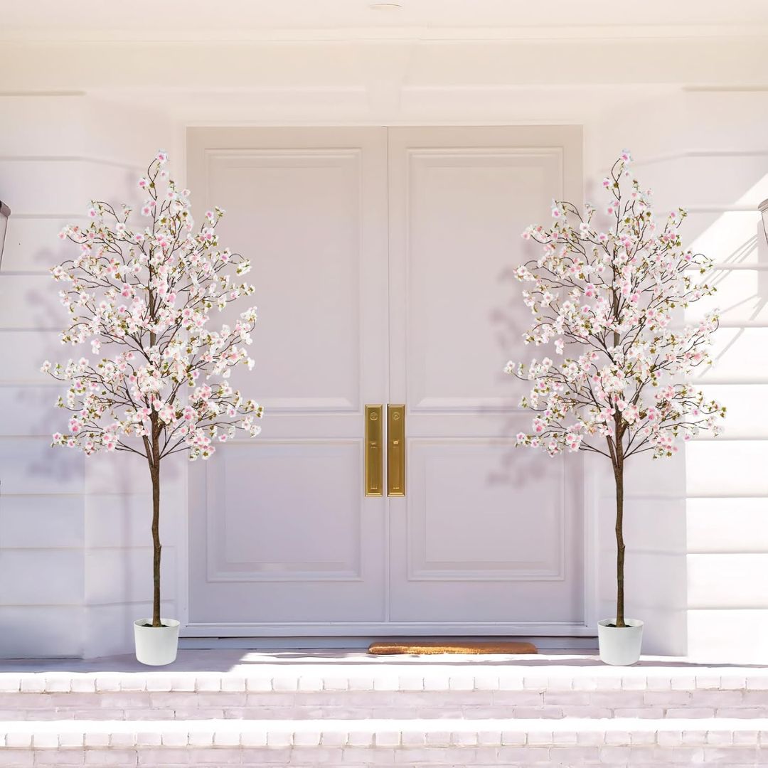 Two artificial cherry blossom trees in front of a white door with gold handles.