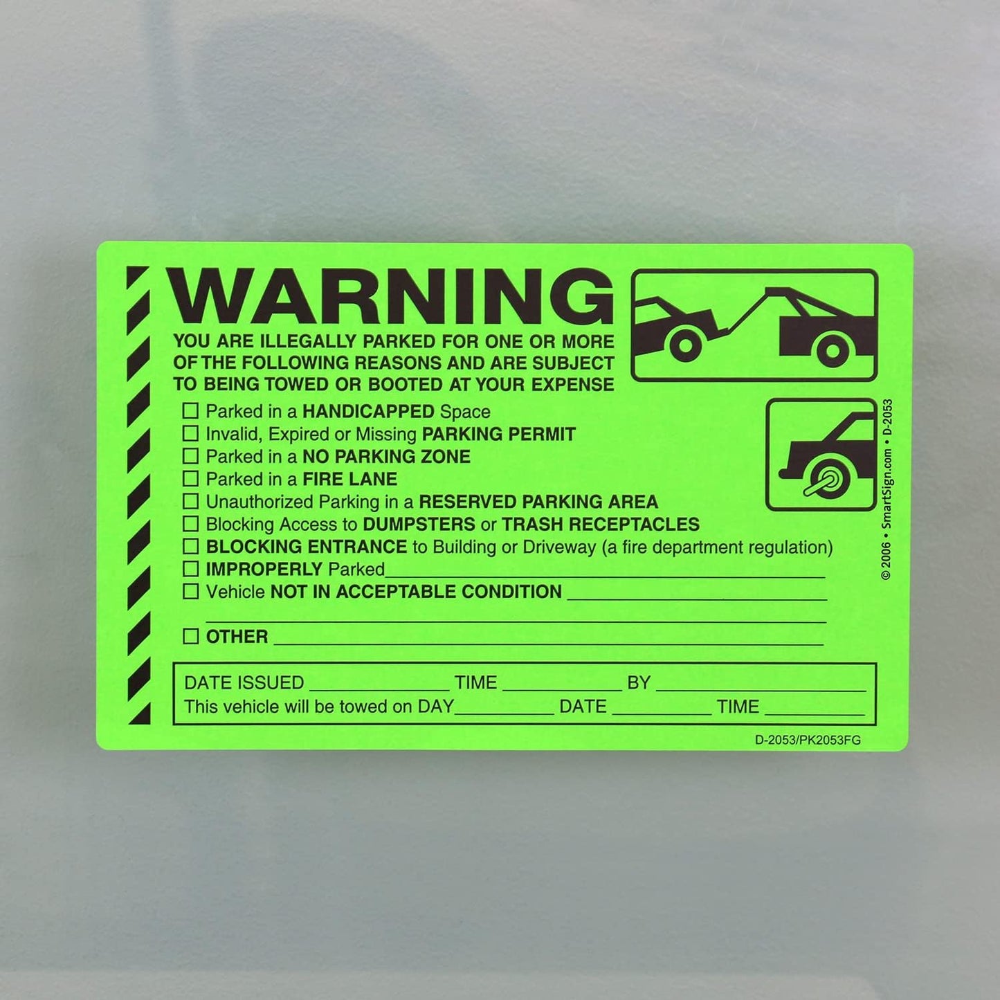 Bright green parking violation warning sticker with checkboxes for various infractions and towing notice details, stuck on a gray surface.