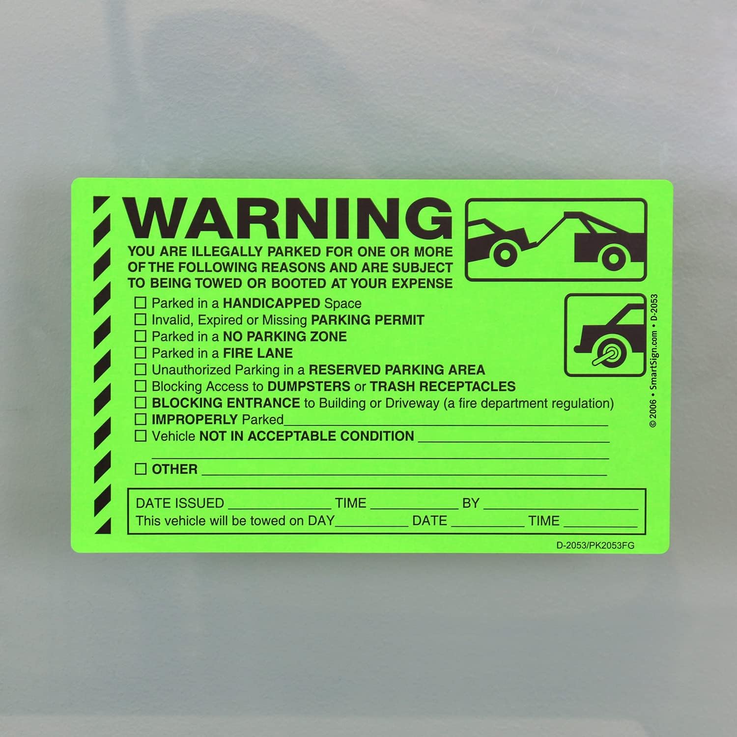 Bright green parking violation warning sticker with checkboxes for various infractions and towing notice details, stuck on a gray surface.