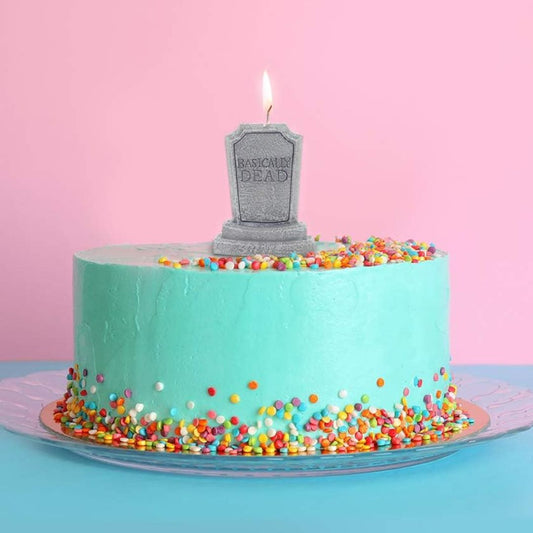 Turquoise cake with colorful sprinkles and a 'Basically Dead' tombstone candle on a pink background