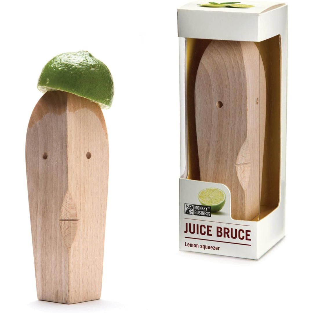Wooden citrus squeezer with a face-like design, shown with a lime on top and in its packaging labeled "Juice Bruce Lemon Squeezer."
