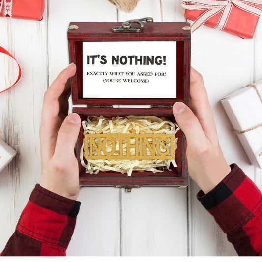 Wooden box with shredded paper labeled 'IT'S NOTHING!' on a white wooden surface.