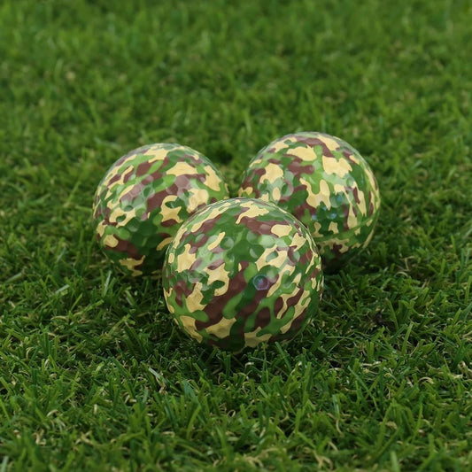 Three camouflage-patterned golf balls on a grassy surface