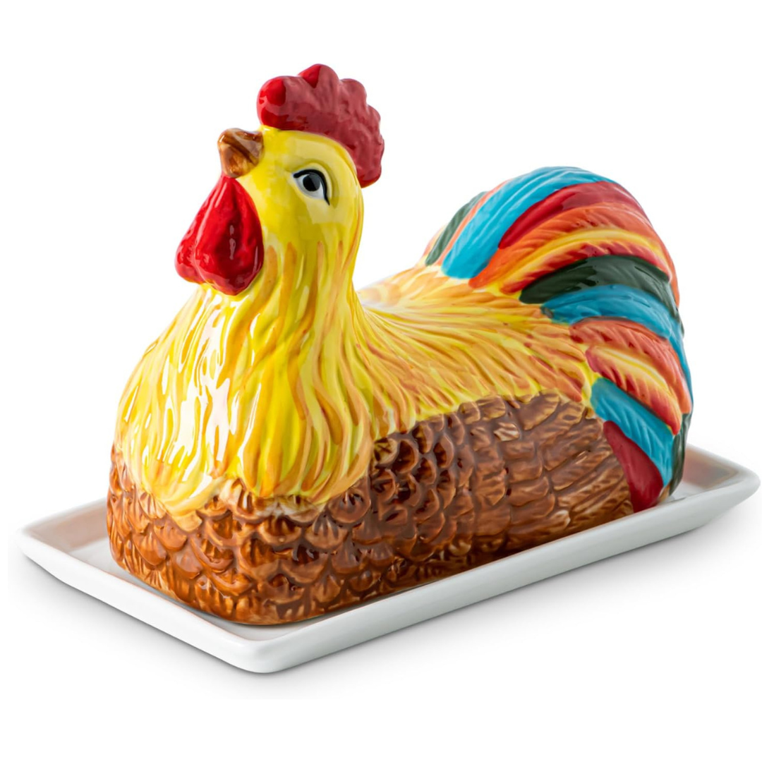 Colorful ceramic butter dish shaped like a chicken with a red comb, yellow body, and vibrant tail feathers, placed on a white rectangular tray.