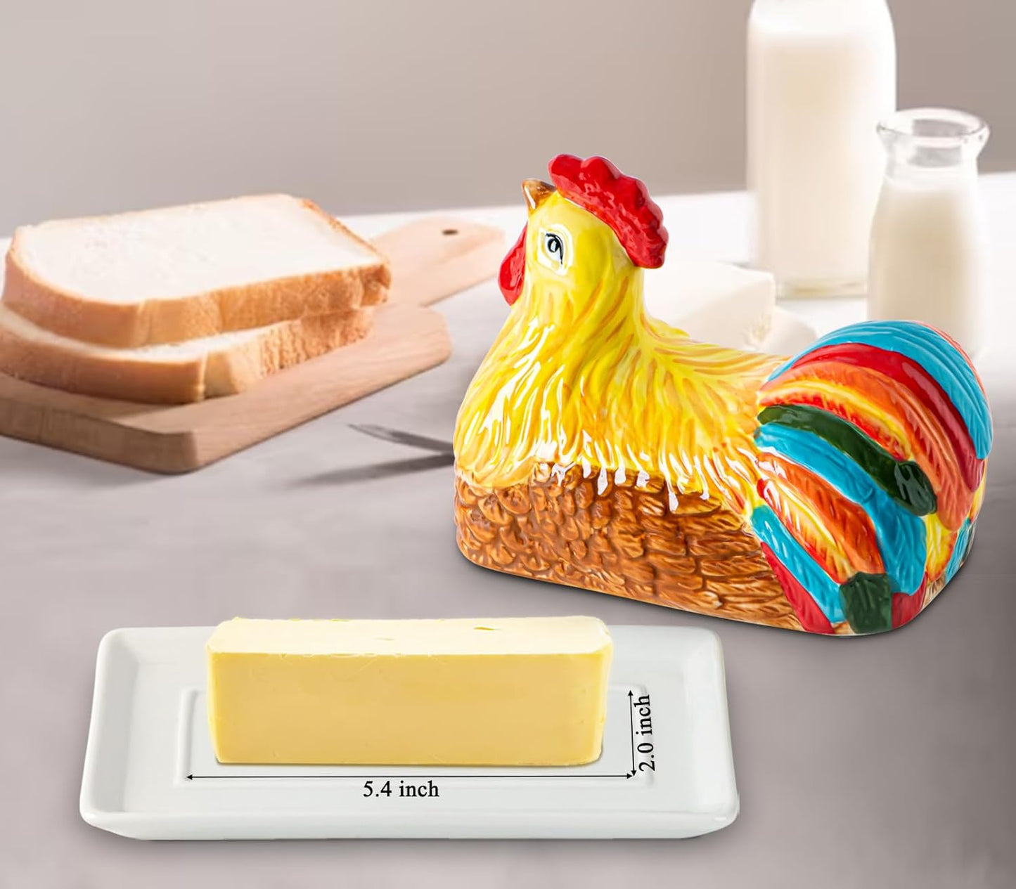 Colorful ceramic chicken-shaped butter dish on a white tray (5.4 x 2.0 inches) with a butter stick, bread on a cutting board, and milk bottles in the background.