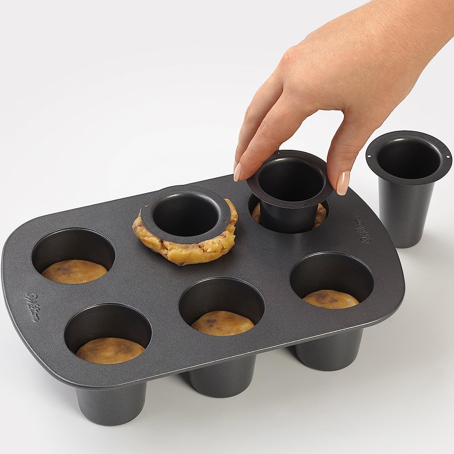 A cookie shot glass baking pan. A person's hand is using the pan to make cookie shot glasses.