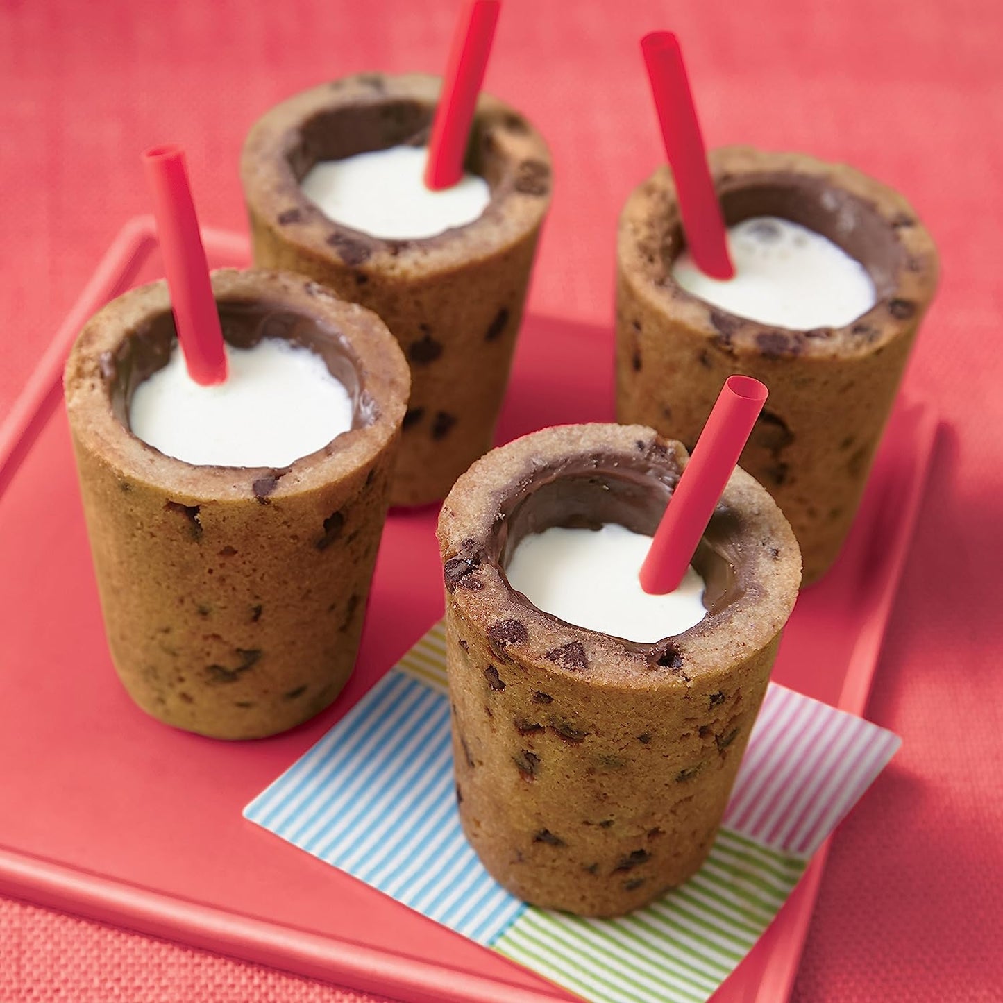 Four shot glasses made from cookie dough filled with a white liquid. Each shot glass has a red straw in it.