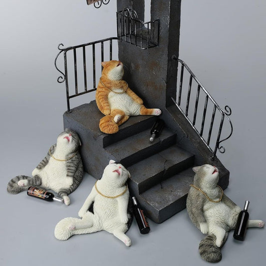 Four resin drunk cat figurines posed around a miniature dark staircase set on a light gray background. One orange-and-white cat sits on the stairs, while three white-and-gray cats lie on the floor beside small bottles.