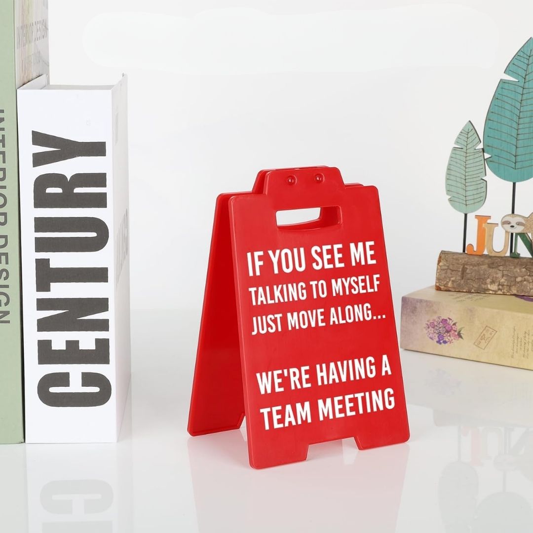 Red sign with humorous text on a white surface with books and decor items.