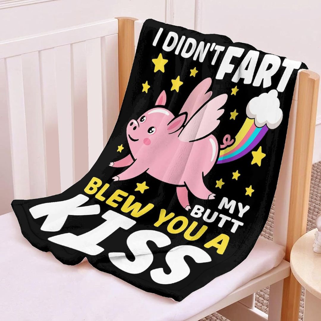 A black blanket featuring a pink flying pig with text that reads "I didn't fart my butt blew you a kiss" spread out on a wooden bench.