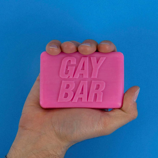 Pink bar of soap with 'GAY BAR' text held in a hand against a blue background