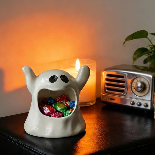 Ceramic ghost-shaped container with colorful candies on a table with a candle and radio in the background.