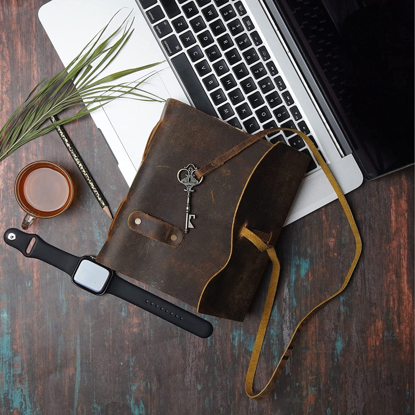 A brown leather vintage journal with key resting on a laptop.
