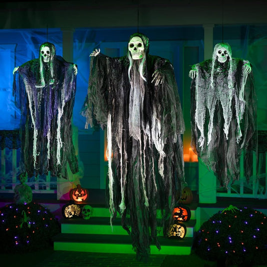 Three hanging Halloween ghost decorations with skull faces and tattered black-and-white robes displayed on a porch with lit pumpkins and blue/green ambient lighting.