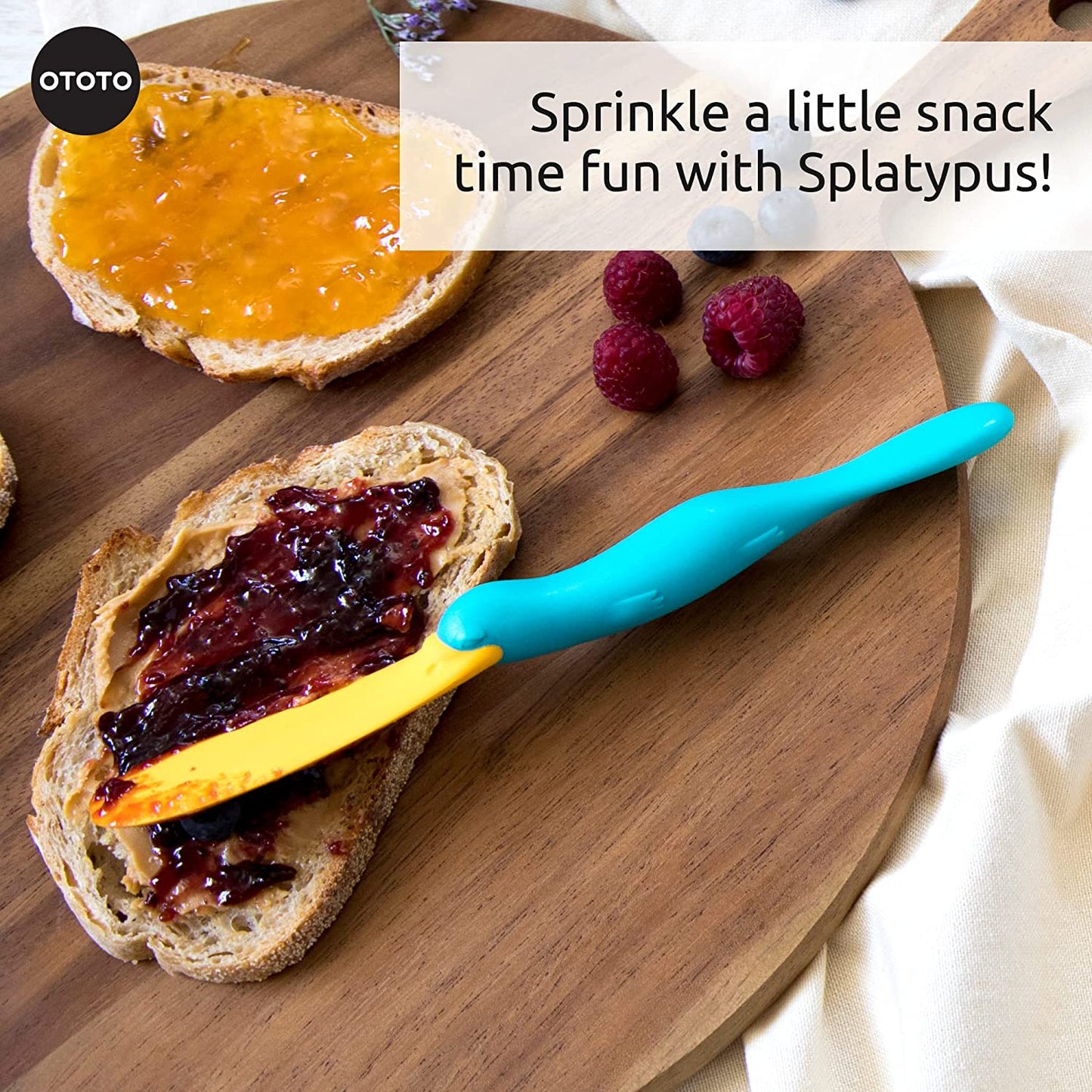 A kitchen scraper spatula called Splatypus is resting on a piece of toast covered in jam on a wooden platter.
