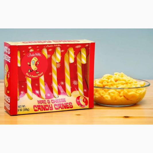 Box of Mac & Cheese Candy Canes next to a bowl of macaroni and cheese on a wooden surface.