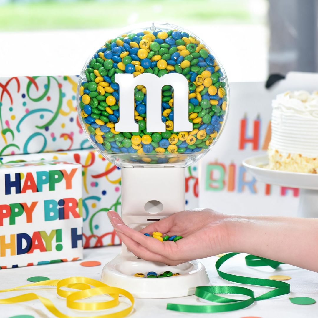 M&Mβs candy dispenser filled with blue, green and yellow chocolates at a colorful birthday party