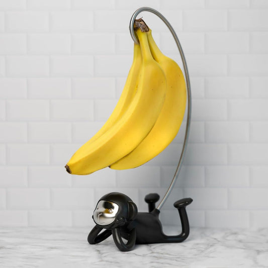 Black monkey-shaped banana holder with bananas on a white marble surface