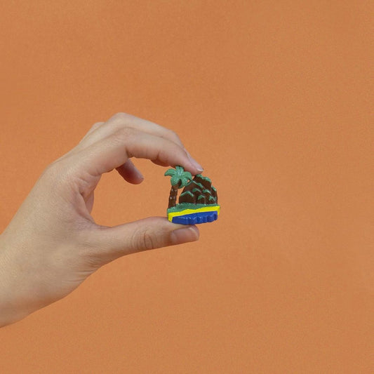Hand holding a small, colorful miniature island against an orange background