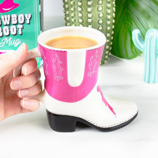 Pink and white cowboy boot mug with a hand holding it, cactus in the background