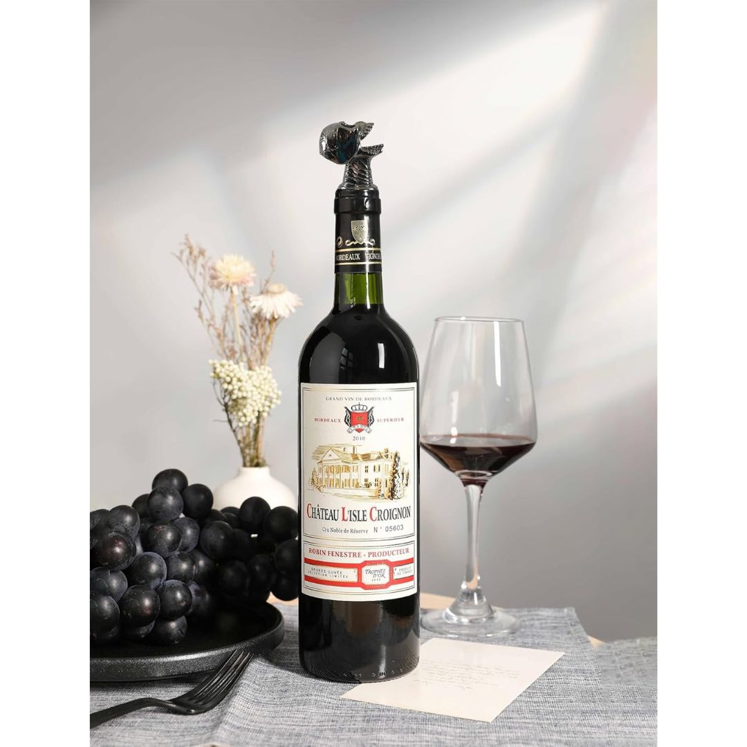 Wine bottle with a black skull shaped aerator and glass of red wine on a table with grapes and flowers.