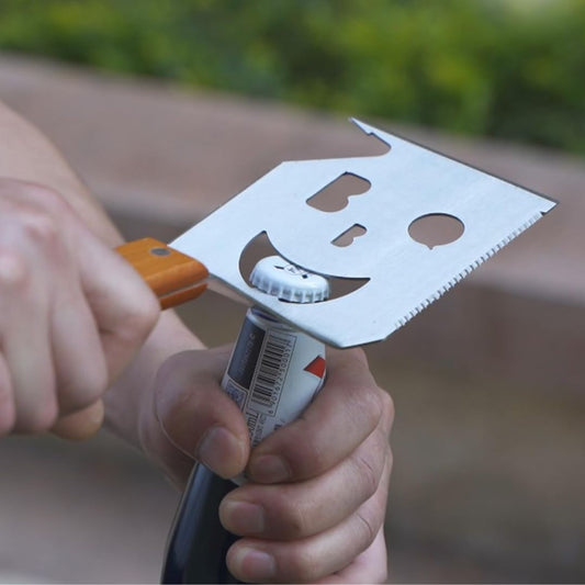 A BBQ tool removing a bottle-top from a bottle.