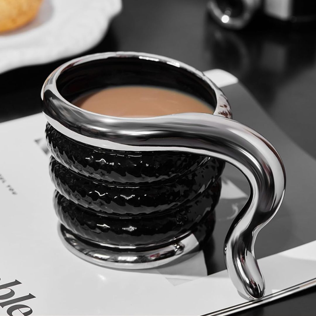 Silver and black snake shaped coffee cup with a handle on a book.