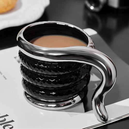 Silver and black snake shaped coffee cup with a handle on a book.