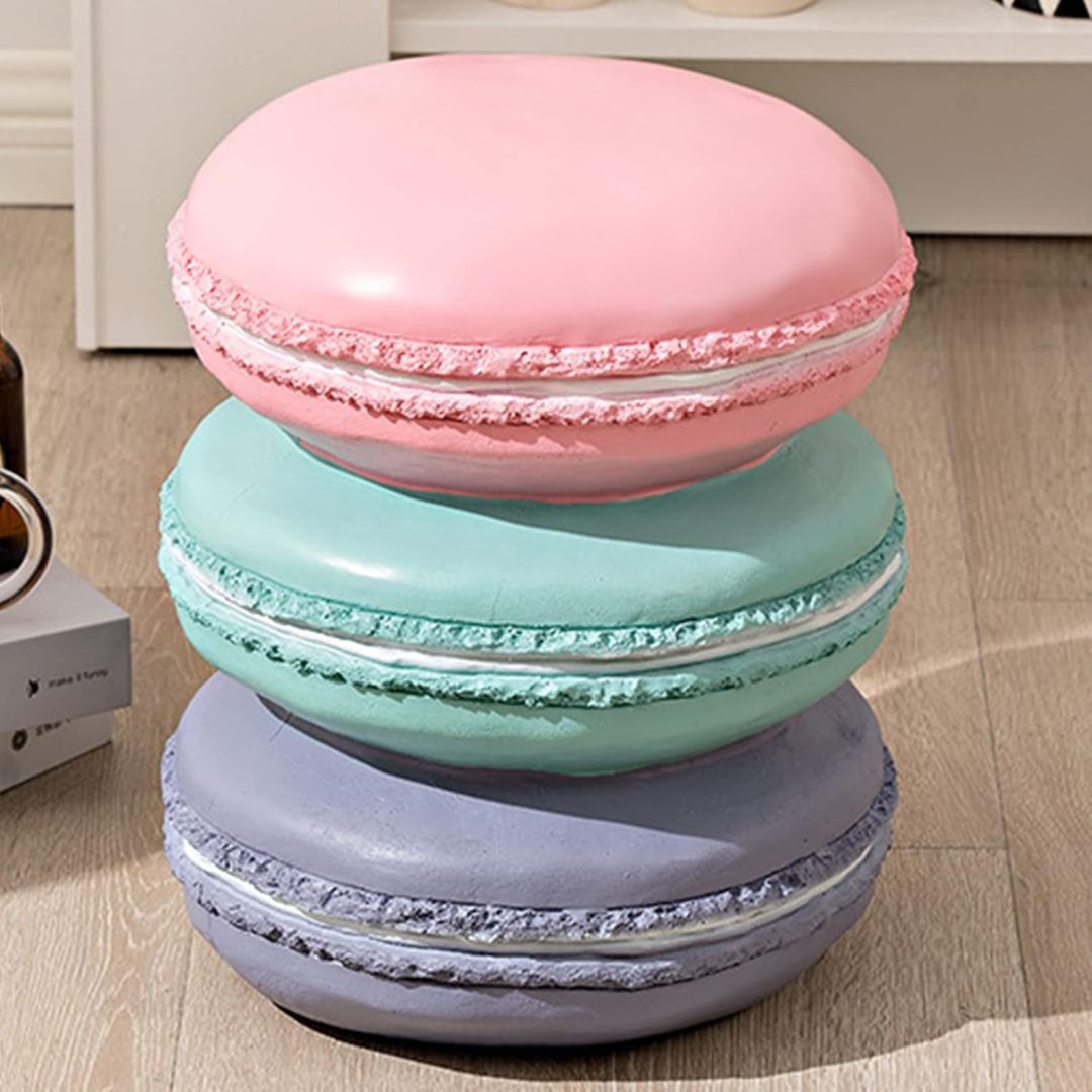 An ottoman shaped as three stacked macarons in pastel pink, mint green, and lavender on a light wood floor.