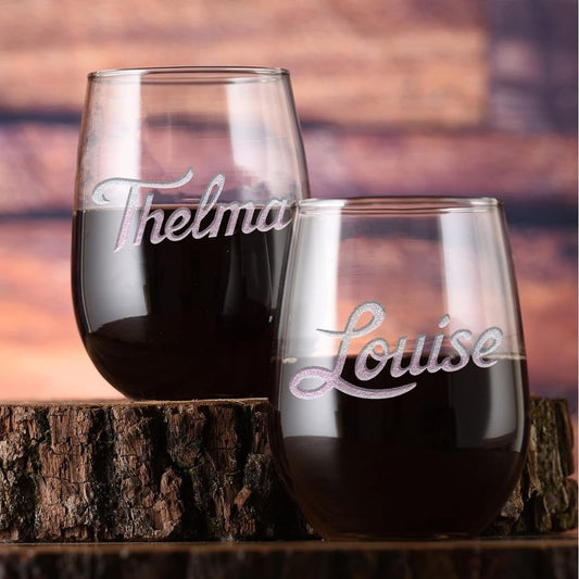 Two stemless wine glasses with 'Thelma' and 'Louise' engraved on them, filled with red wine, against a wooden background.