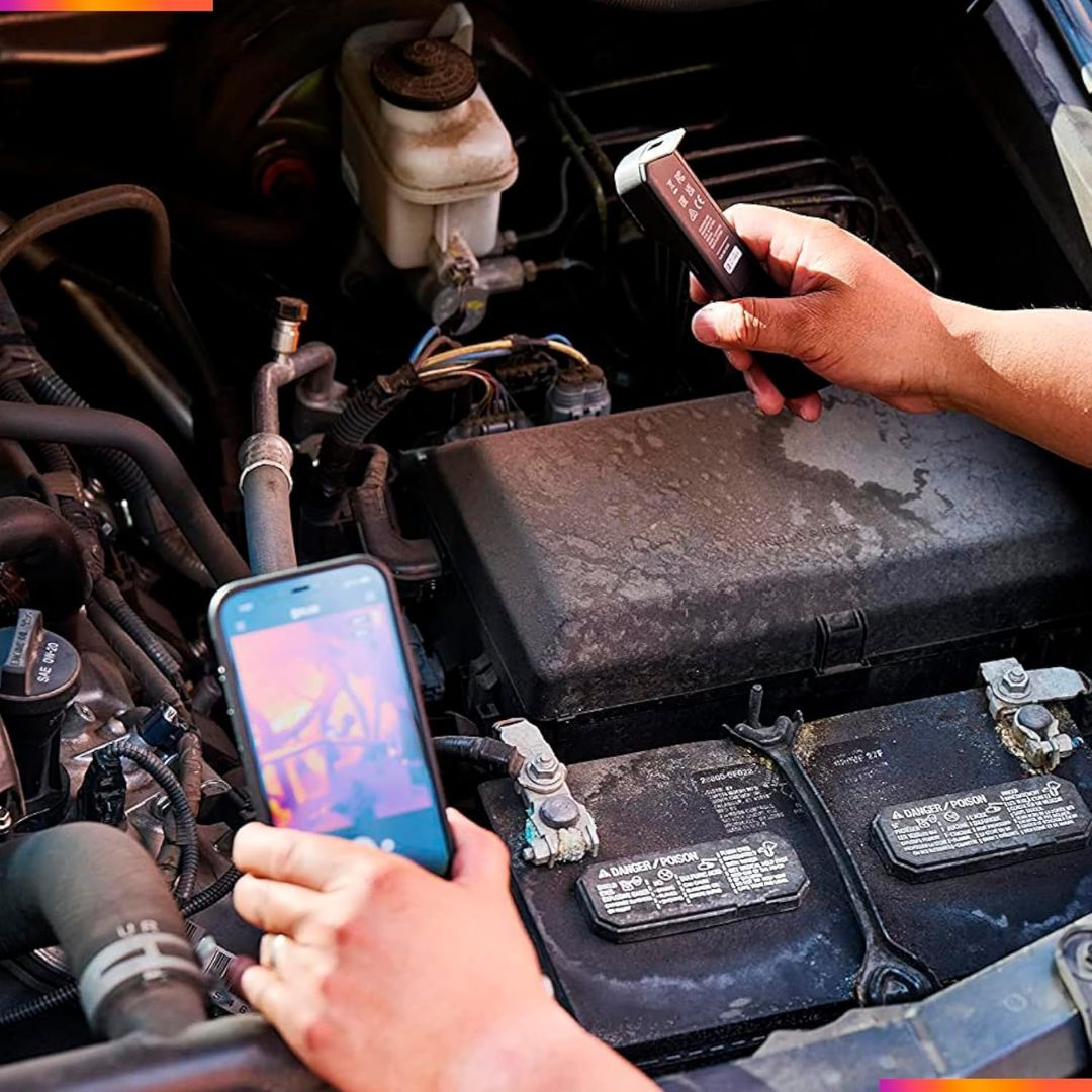 A person is using a black wireless thermal imaging camera while looking at an engine under a cars hood