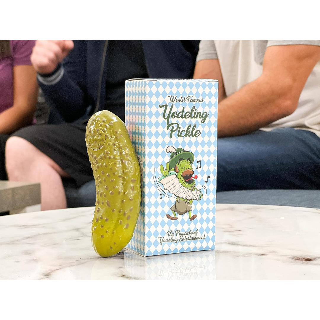 Yodeling pickle toy and box on a marble table with people sitting on a couch in the background.