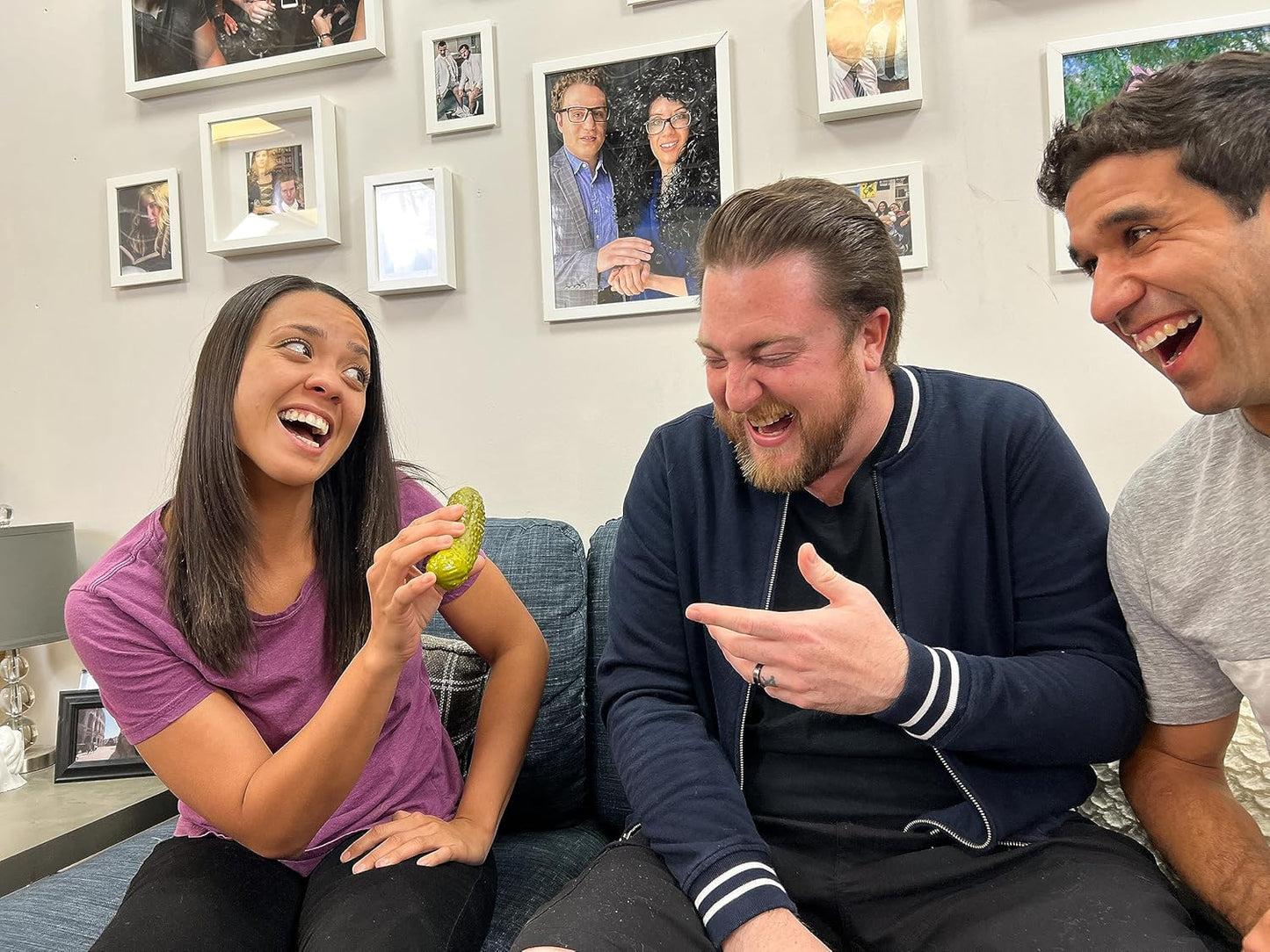 A woman is holding a yodelling pickle while two men laugh.
