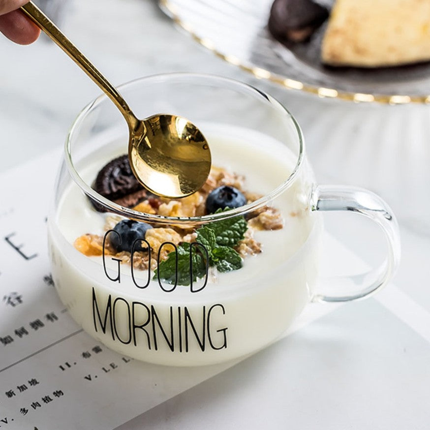 A glass mug holding milk and cereal with a gold spoon