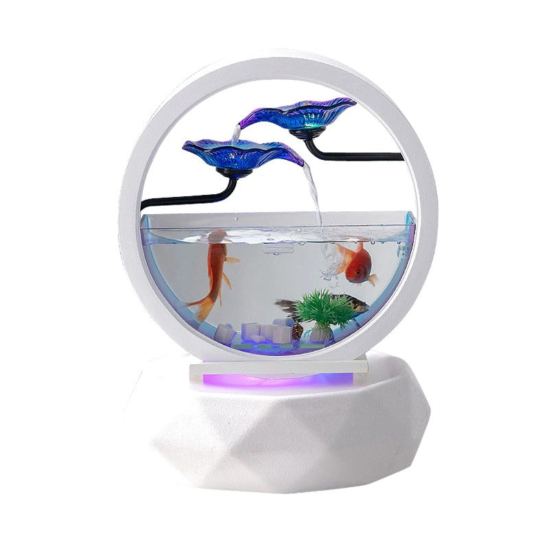 A decorative aquarium which also features a waterfall and an air purifier. There are 3 gold fish swimming inside. This fish tank features two blue glass flowers on top and water is cascading down the flowers and into the aquarium. The base of this fish tank is an air purifier. The aquarium is white and circular and so is the base.