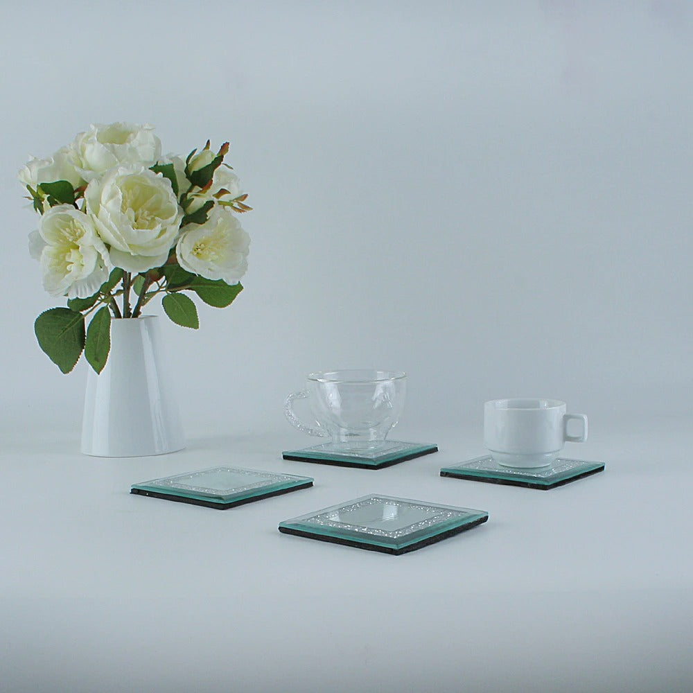 Four crystal coasters with each coaster filled with tiny rhinestone crystals. There are cups on two of the coasters and a bunch of white flowers nearby.