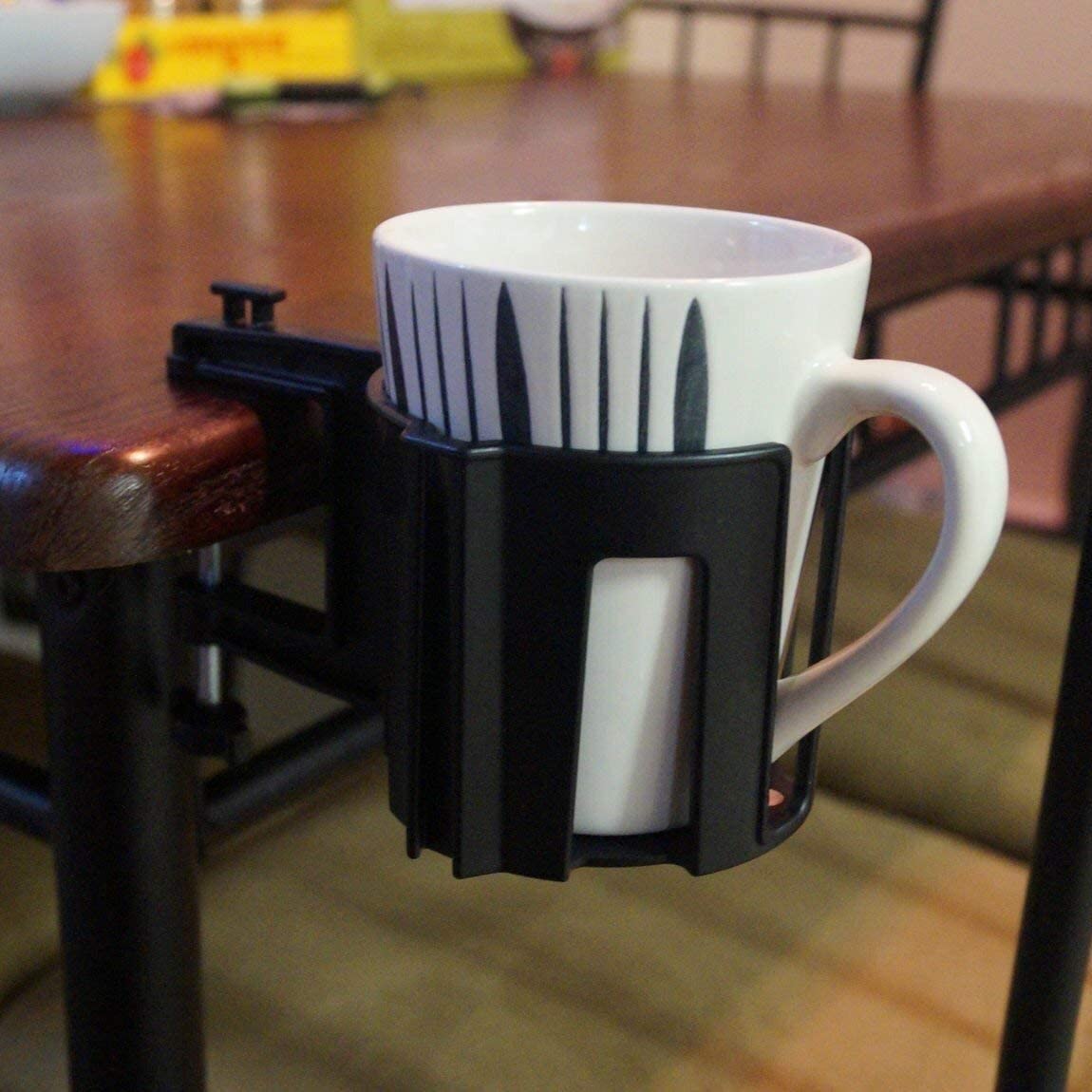 A cup holster attached to a wooden desk. A white mug is inside the holster.