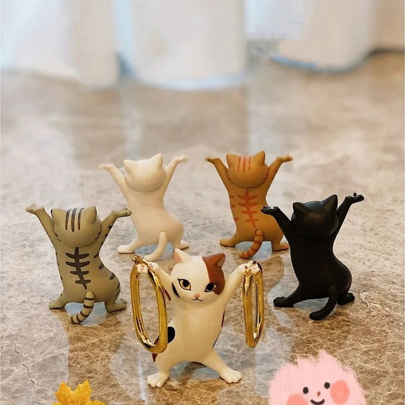 Five dancing cat figures. Four of them have their back to the camera and the one facing forward is holding a pair of earrings.