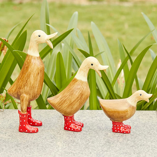 Three garden decors made out of wood with each one wearing red colored Wellington boots with white spots.