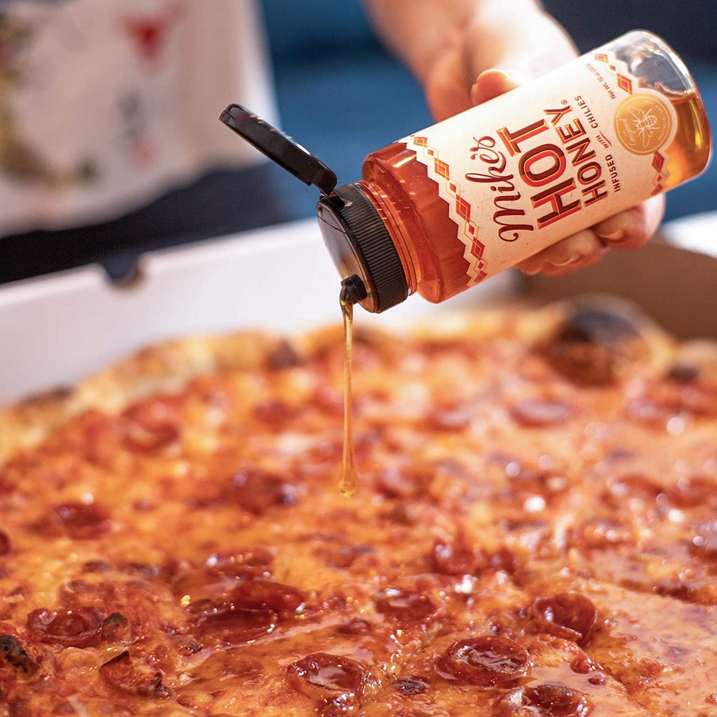 Someone is holding a squeeze bottle of Mike's hot honey and pouring it on a pizza.