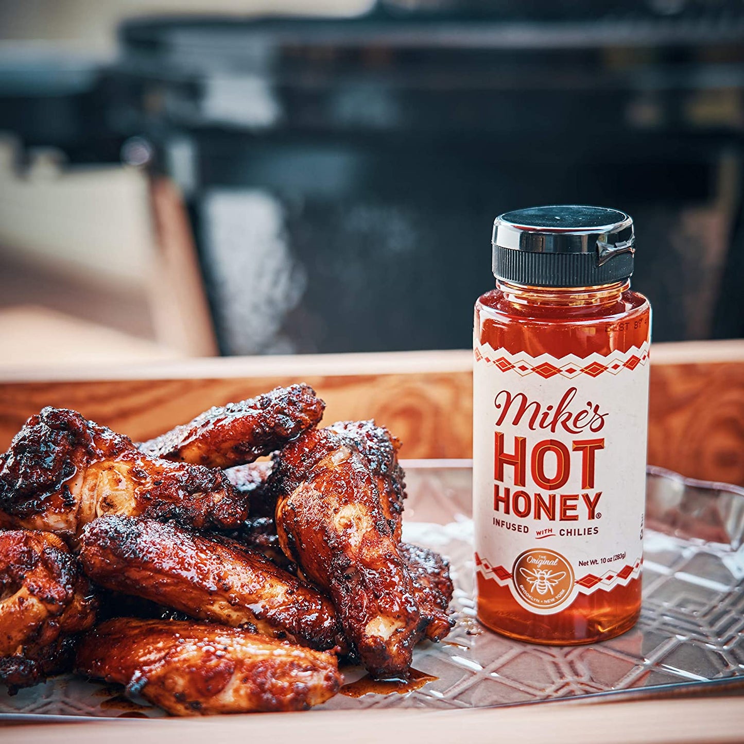 A jar of Mike's hot honey is next to a pile of cooked chicken wings.