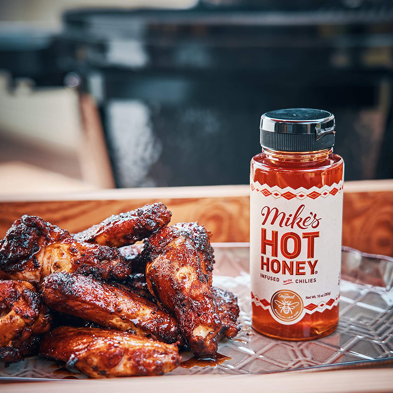 A jar of Mike's hot honey is next to a pile of cooked chicken wings.