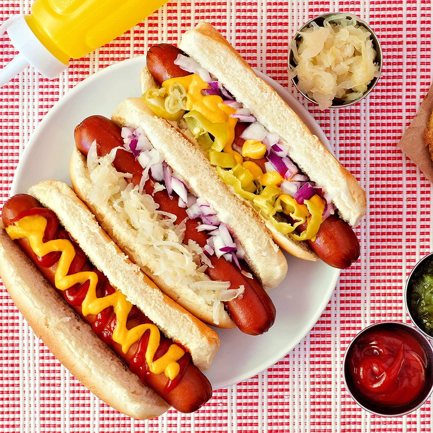 A plate filled with 3 cooked hotdogs in buns all filled with various condiments.