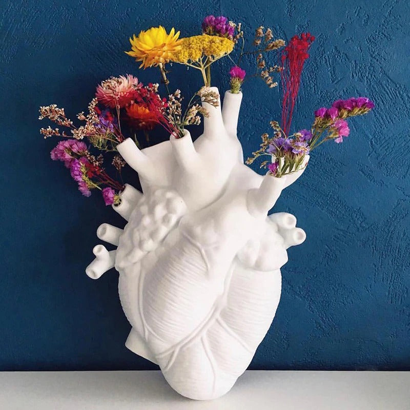 A white human heart shaped vase complete with arteries. The holes of the arteries are filled with various wildflowers.