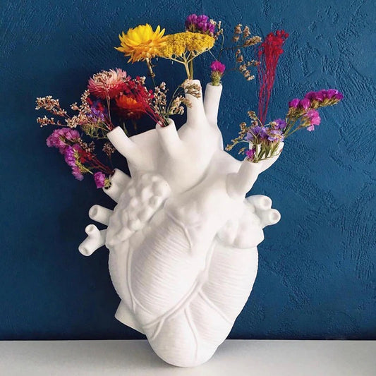 A white human heart shaped vase complete with arteries. The holes of the arteries are filled with various wildflowers.