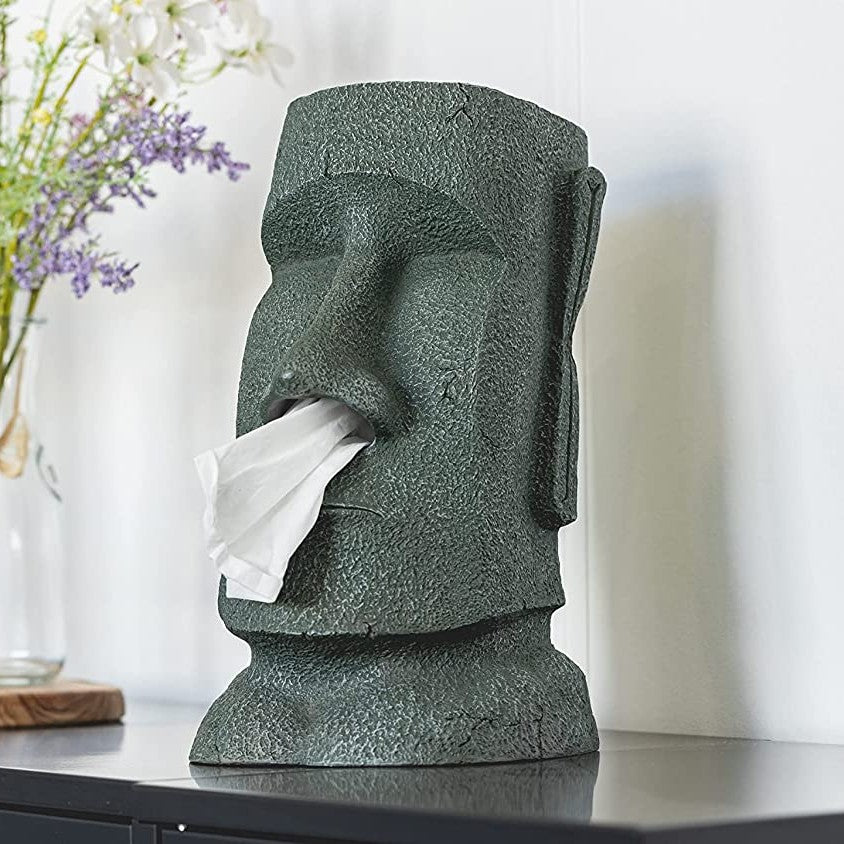 A moai shaped tissue box holder with a tissue hanging out of its nose.