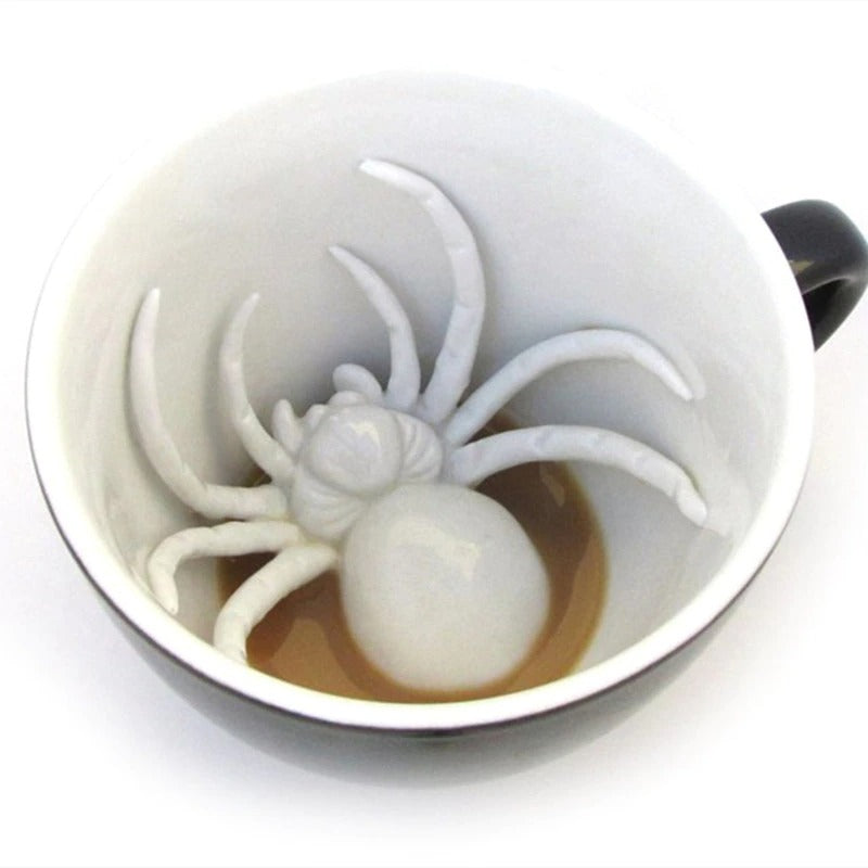 A ceramic coffee and tea cup which has a fake ceramic spider hidden at the bottom of the cup.