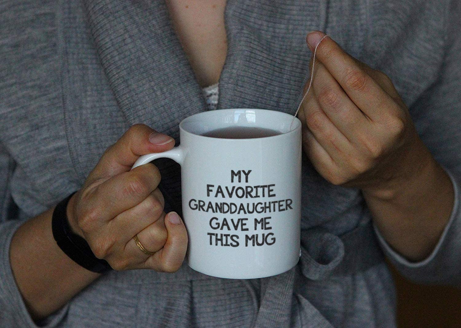 A pair of hands are holding a white ceramic coffee cup with the words, 'my favorite granddaughter gave me this mug' printed on it.