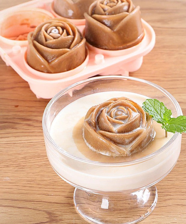An ice cube mold maker which makes rose shaped ice cubes. In the foreground is a fancy champagne glass filled with liquid and features a chocolate colored rose shaped ice cube. In the background sits the rose mold maker with 3 rose shaped ice cubes in it.