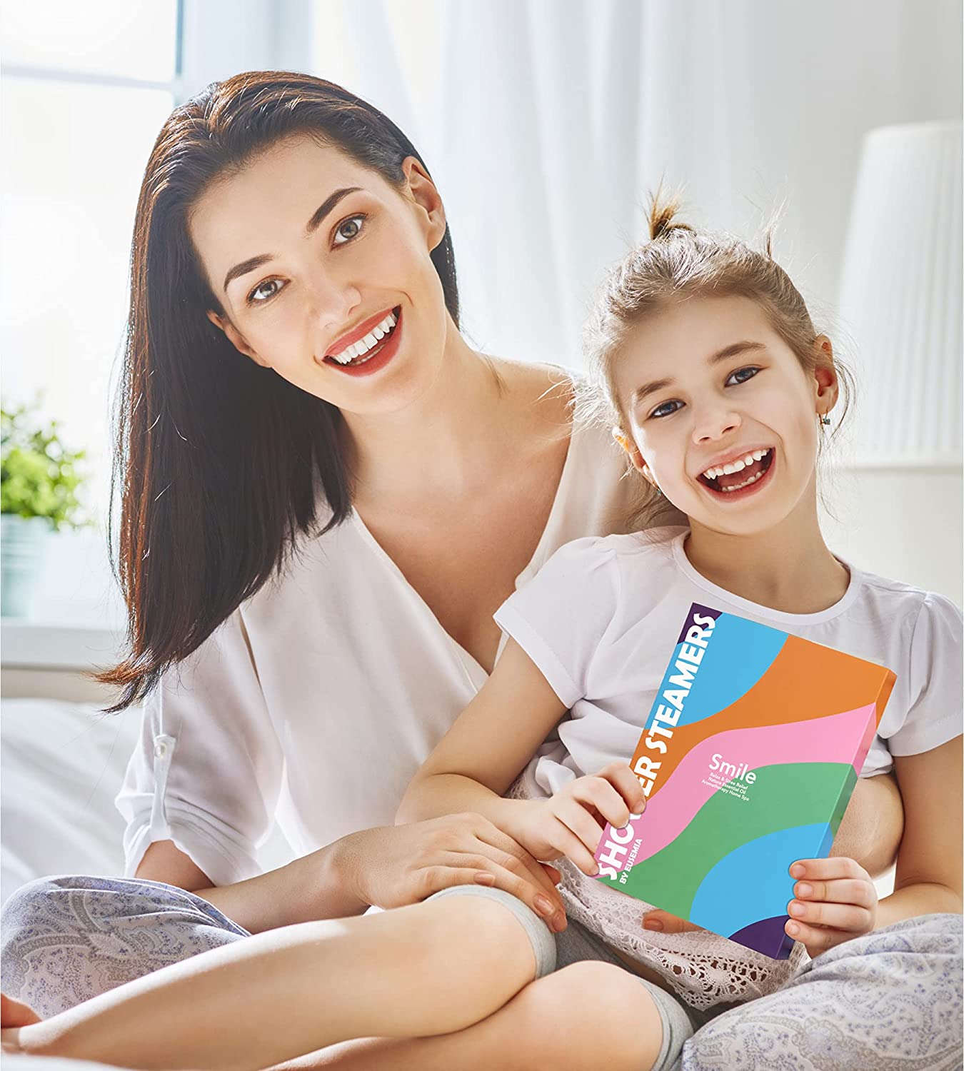 A mother and child are smiling at the camera. The child is holding a gift box of shower bombs.